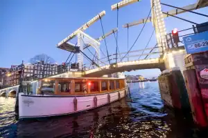 Avondfoto Saloonsloep varend onder brug Amsterdam
