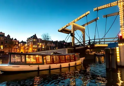 Salonboot das durch eine Br&uuml;cke f&auml;hrt am Abend in Amsterdam
